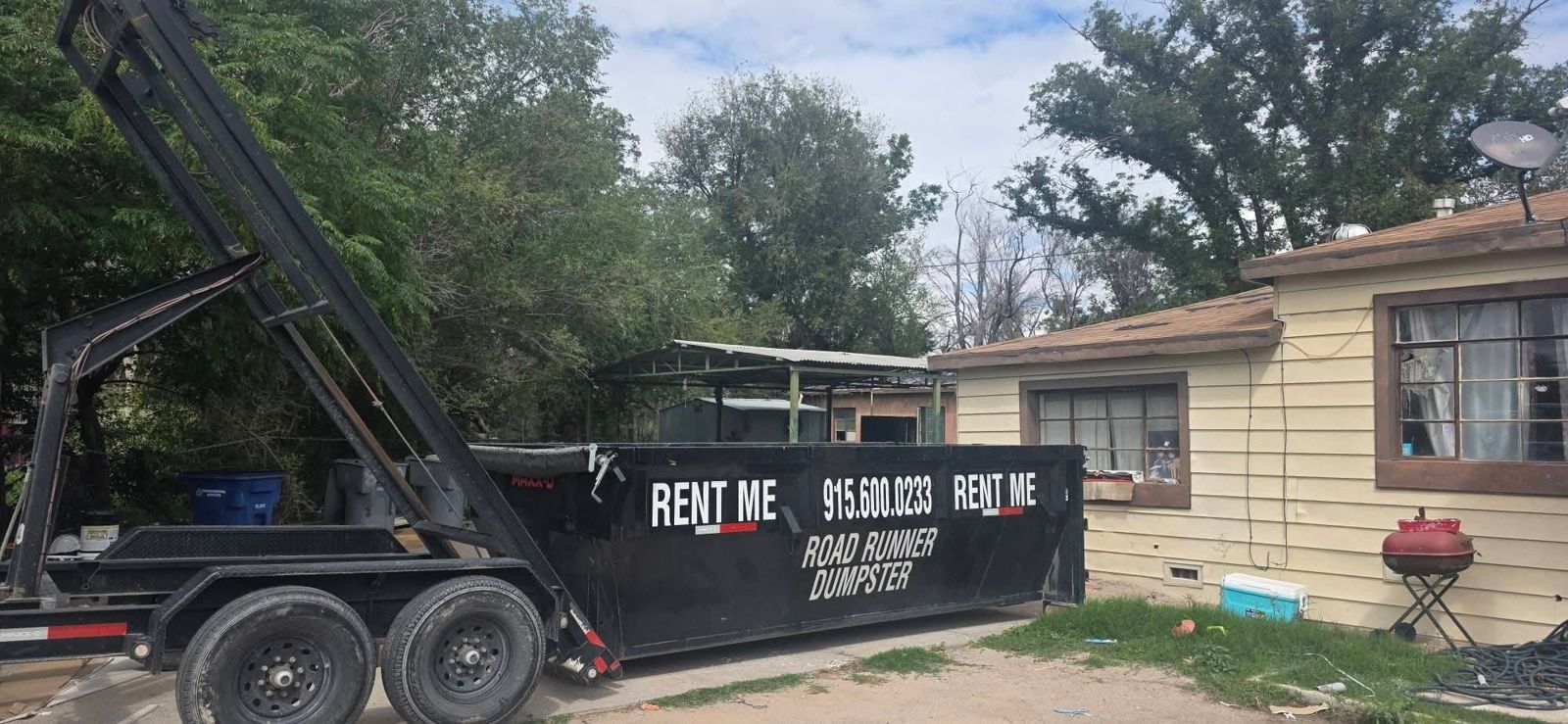 Roadrunner Dumpster container labeled Rent Me 915.600.0233 placed next to a house