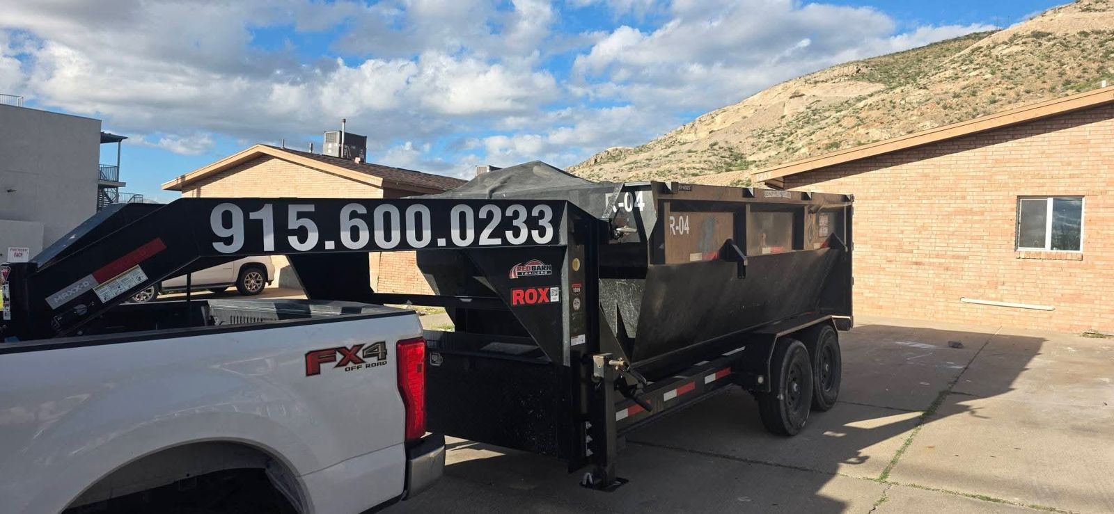 Roadrunner Dumpster truck and black container trailer marked 915.600.0233 parked beside a building